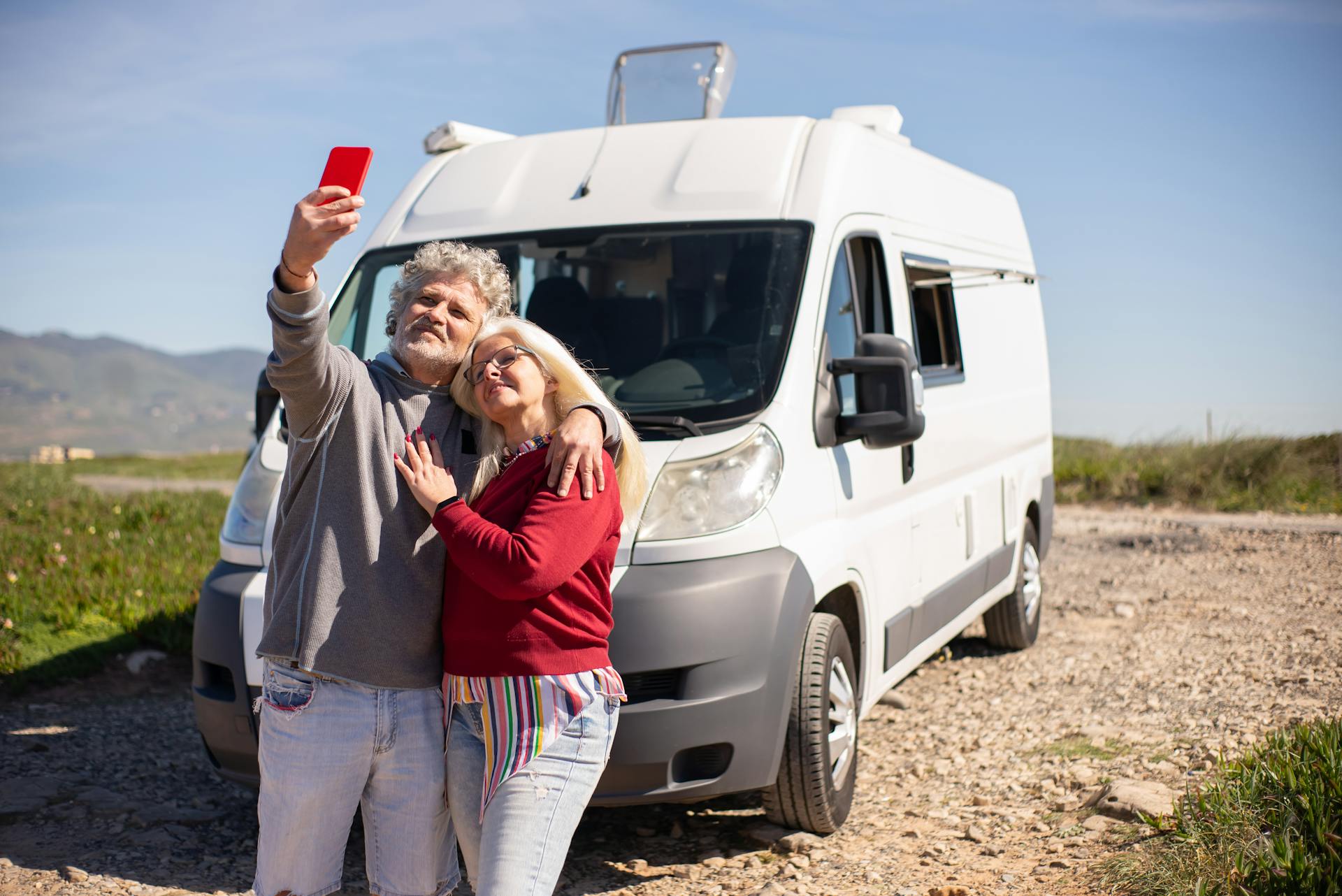 A senior couple taking a selfie with their RV in Portugal, enjoying a sunny travel adventure.