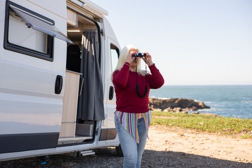 Free Woman enjoying a scenic view by the sea with binoculars near a camper van in Portugal. Stock Photo