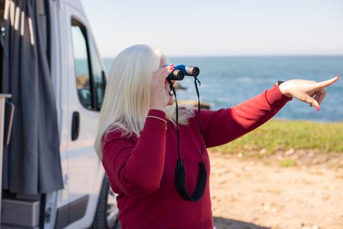 Free Woman using binoculars by the coast in Portugal, observing the ocean. Stock Photo