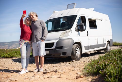 Free Senior couple enjoying a road trip in Portugal, capturing a selfie beside their RV. Stock Photo