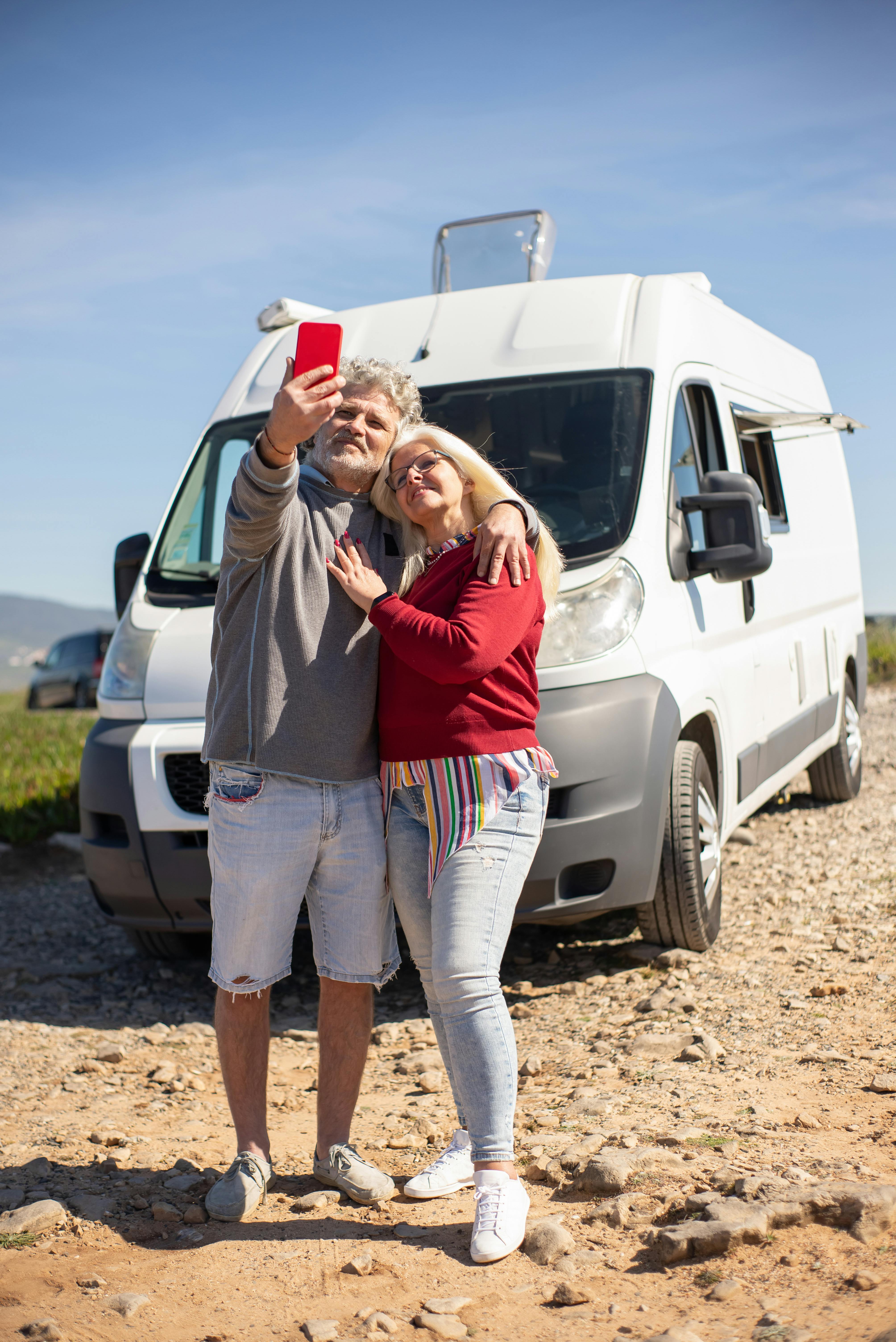 Elderly couple capturing a selfie in front of a white van on a sunny day in Portugal, enjoying the outdoors.