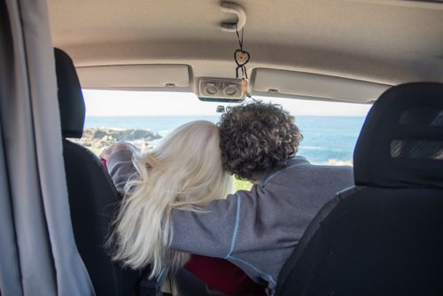 Free Couple embracing inside a campervan with a scenic ocean view, capturing a moment of love and adventure. Stock Photo