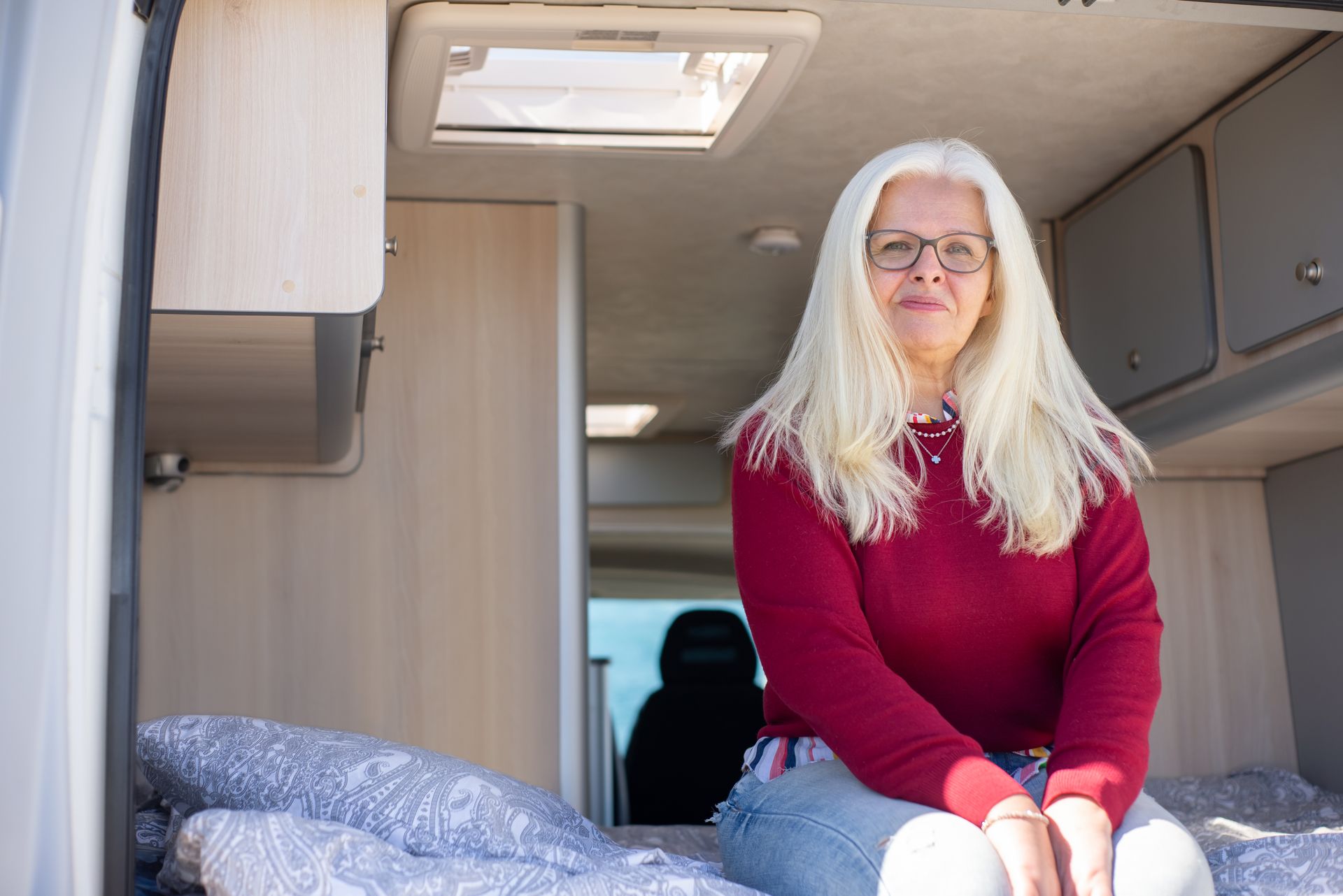 Elderly woman with blonde hair sitting in a campervan, enjoying van life in Portugal.