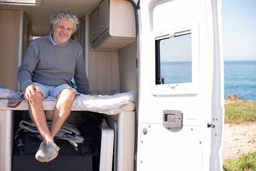 Man Sitting on the Bed in His Motorhome on the Seashore 