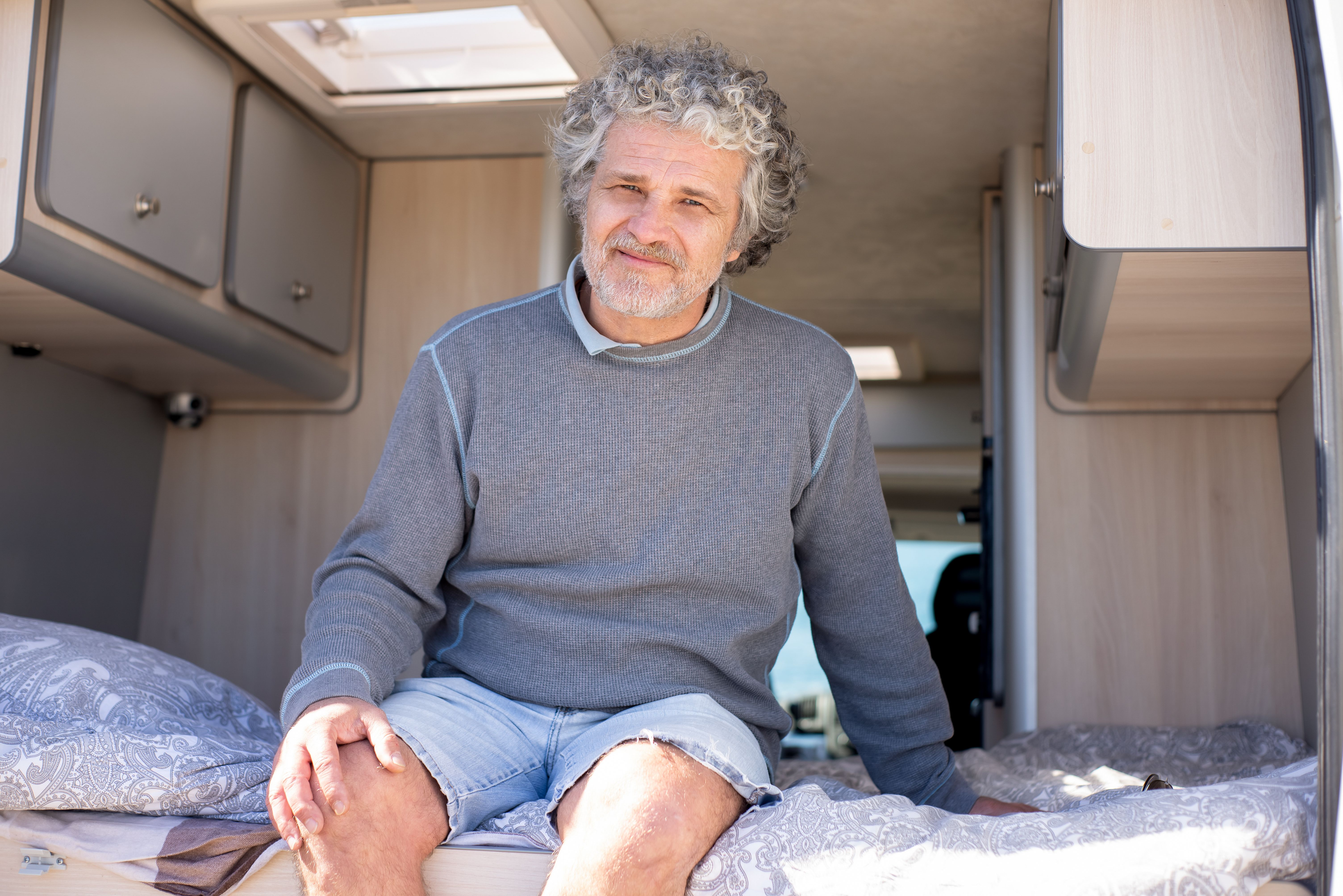 Happy senior man sitting in a cozy camper van interior during a summer trip.