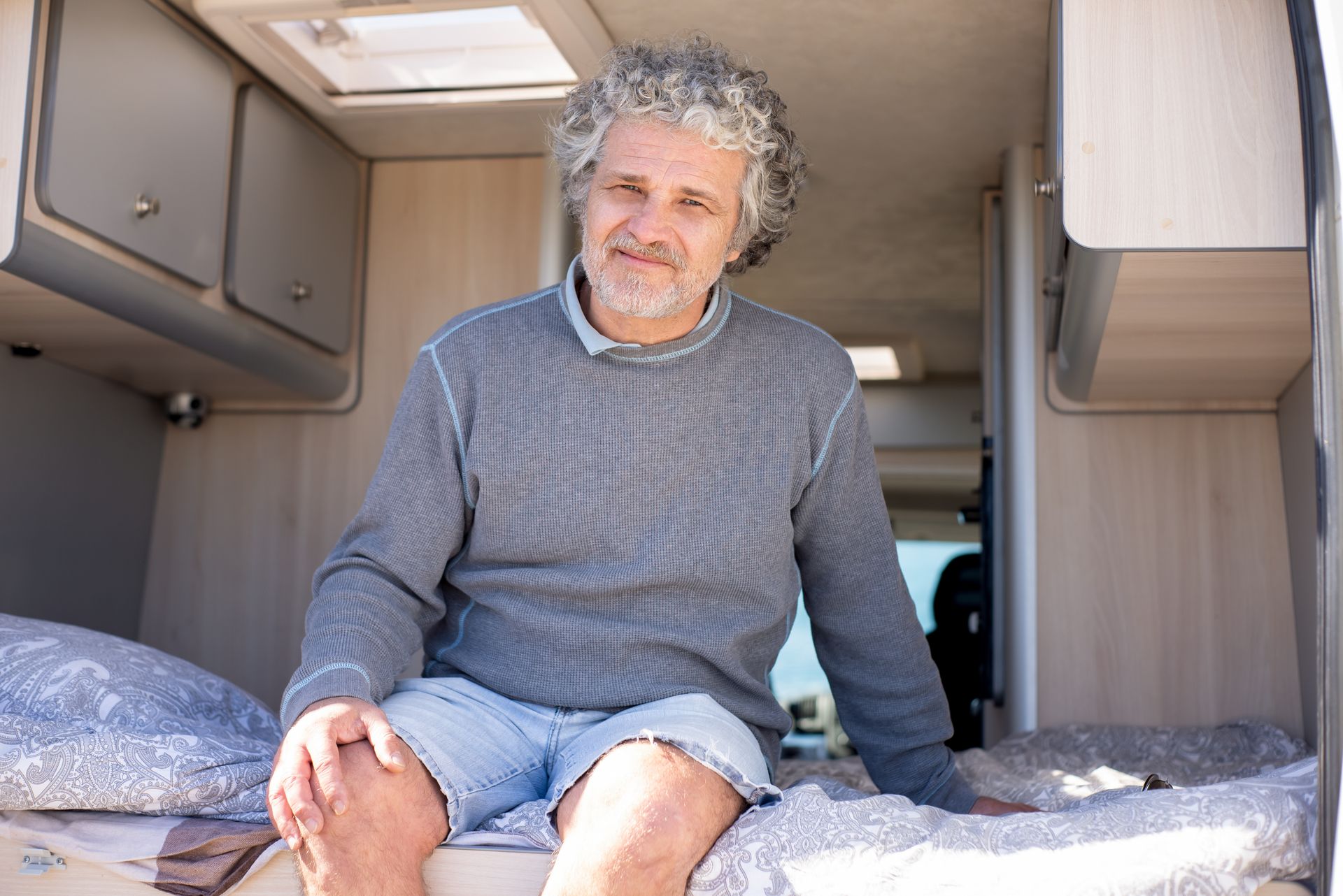 Happy senior man sitting in a cozy camper van interior during a summer trip.