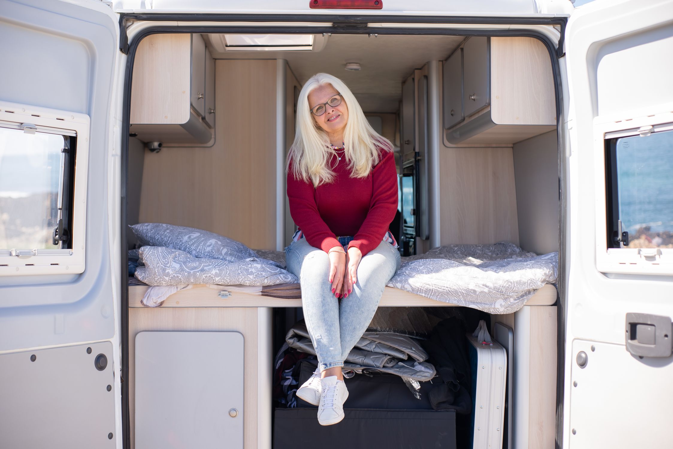 Elderly woman with blonde hair sitting happily in a campervan during a roadtrip in Portugal.