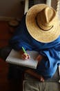 Person Wearing Brown Straw Hat Writing on a Sketchbook