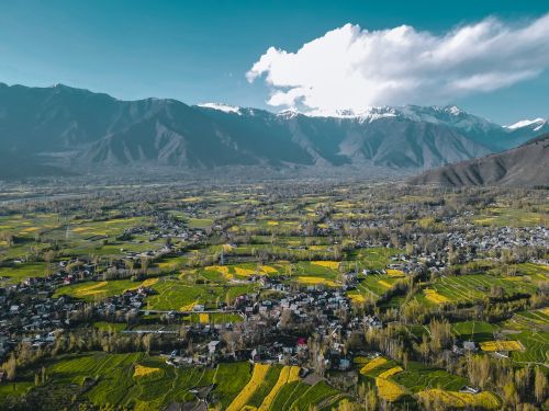 Free Aerial view of a rural village surrounded by fields and snowcapped mountains under a clear sky. Stock Photo