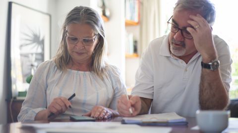 Senior couple calculating expenses at home office desk with documents and notes.