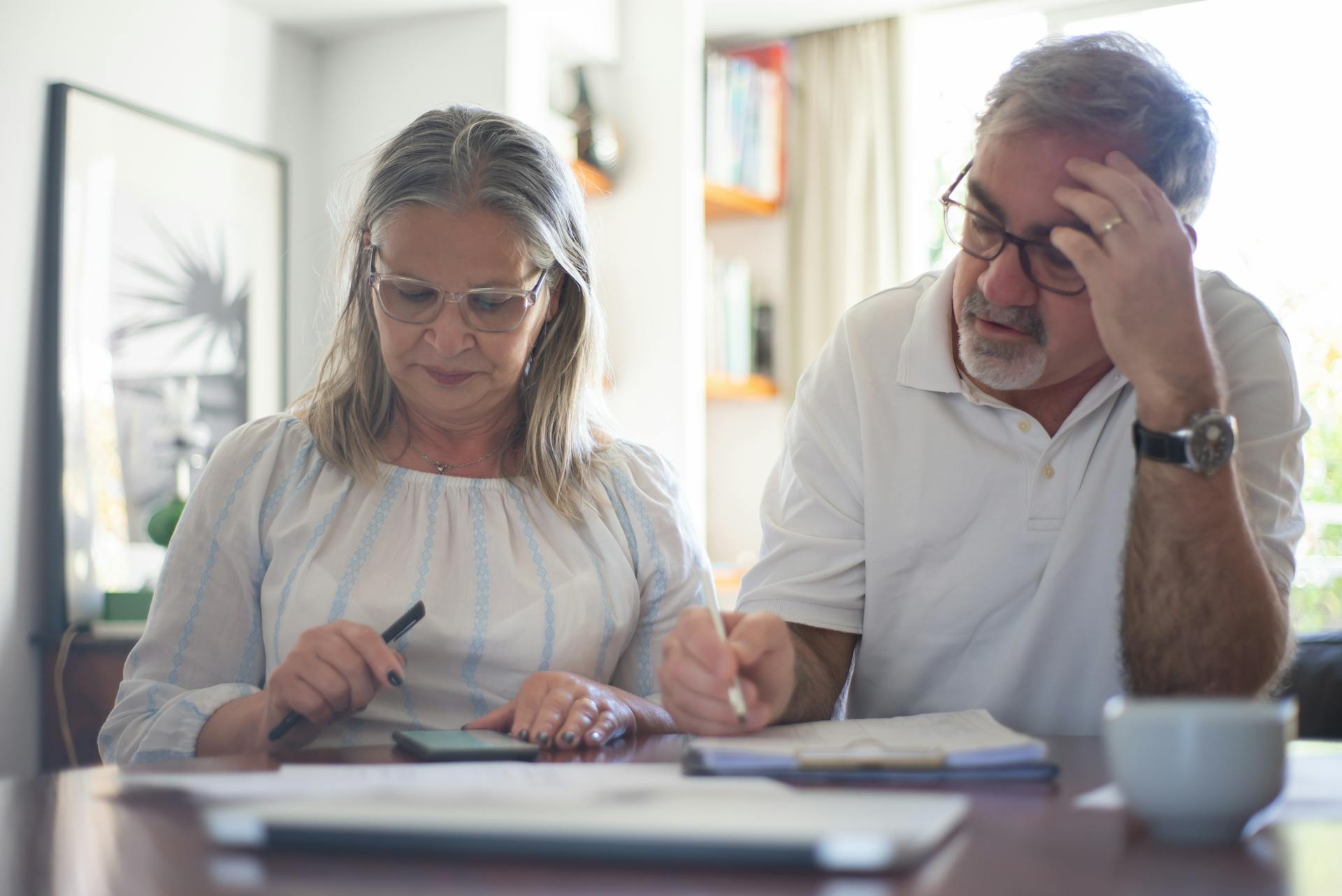 Senior couple calculating expenses at home office desk with documents and notes.