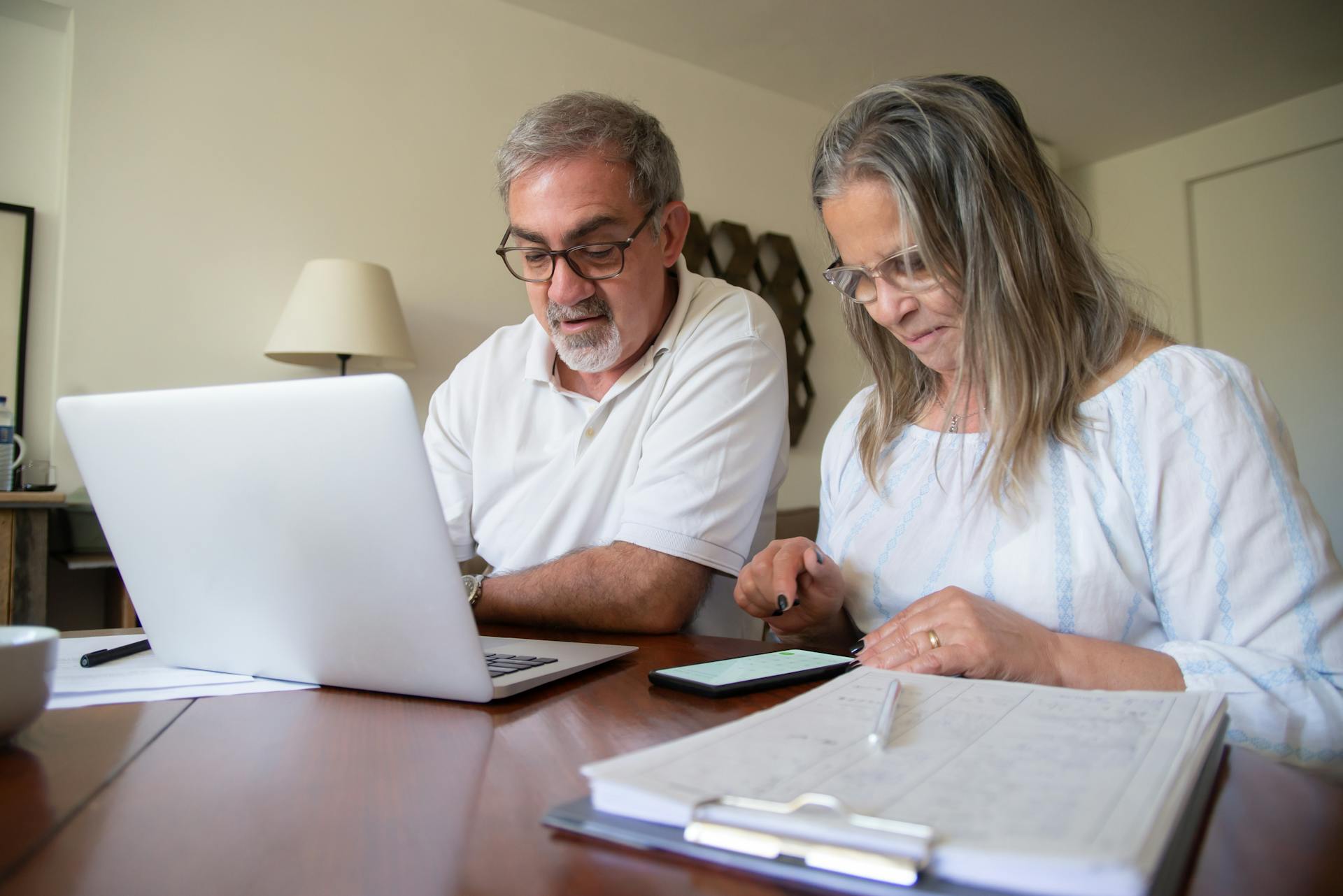 Senior couple working together on documents with laptop and phone at home.