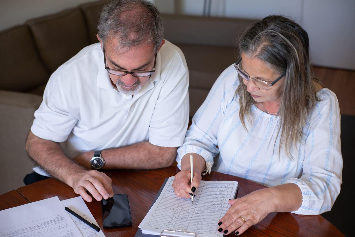 Older couple reviewing financial documents and a smartphone at home