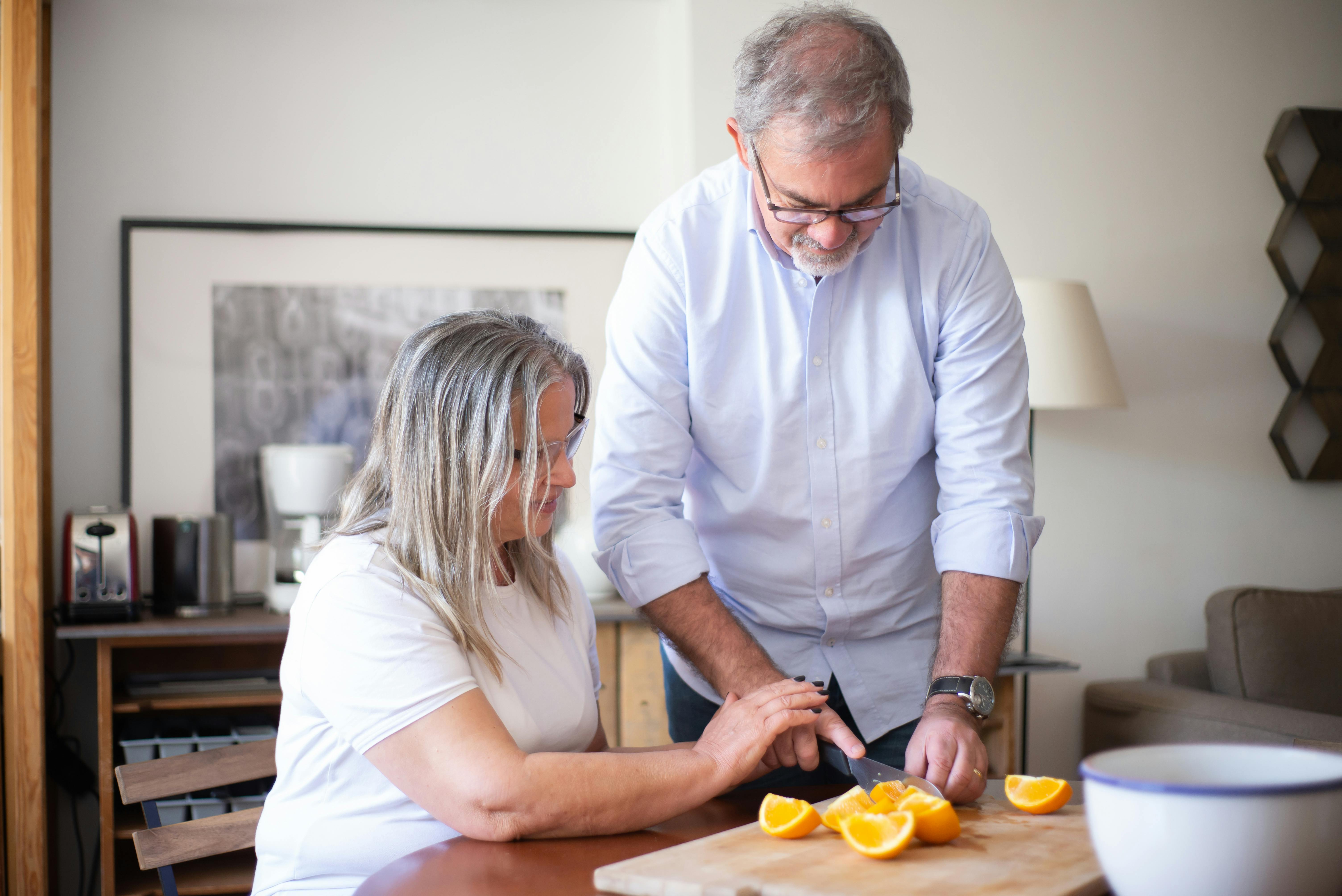 An elderly couple enjoys a moment together, slicing oranges in their cozy home.