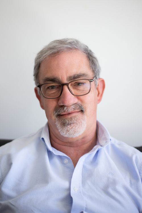 Free Close-up portrait of a smiling mature man with glasses and gray hair, wearing a blue shirt. Stock Photo
