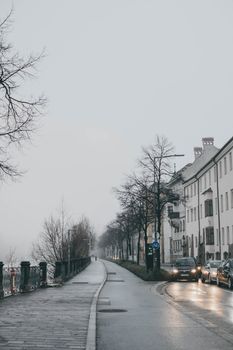 Misty winter street in Austria with leafless trees and urban traffic under a gray sky.