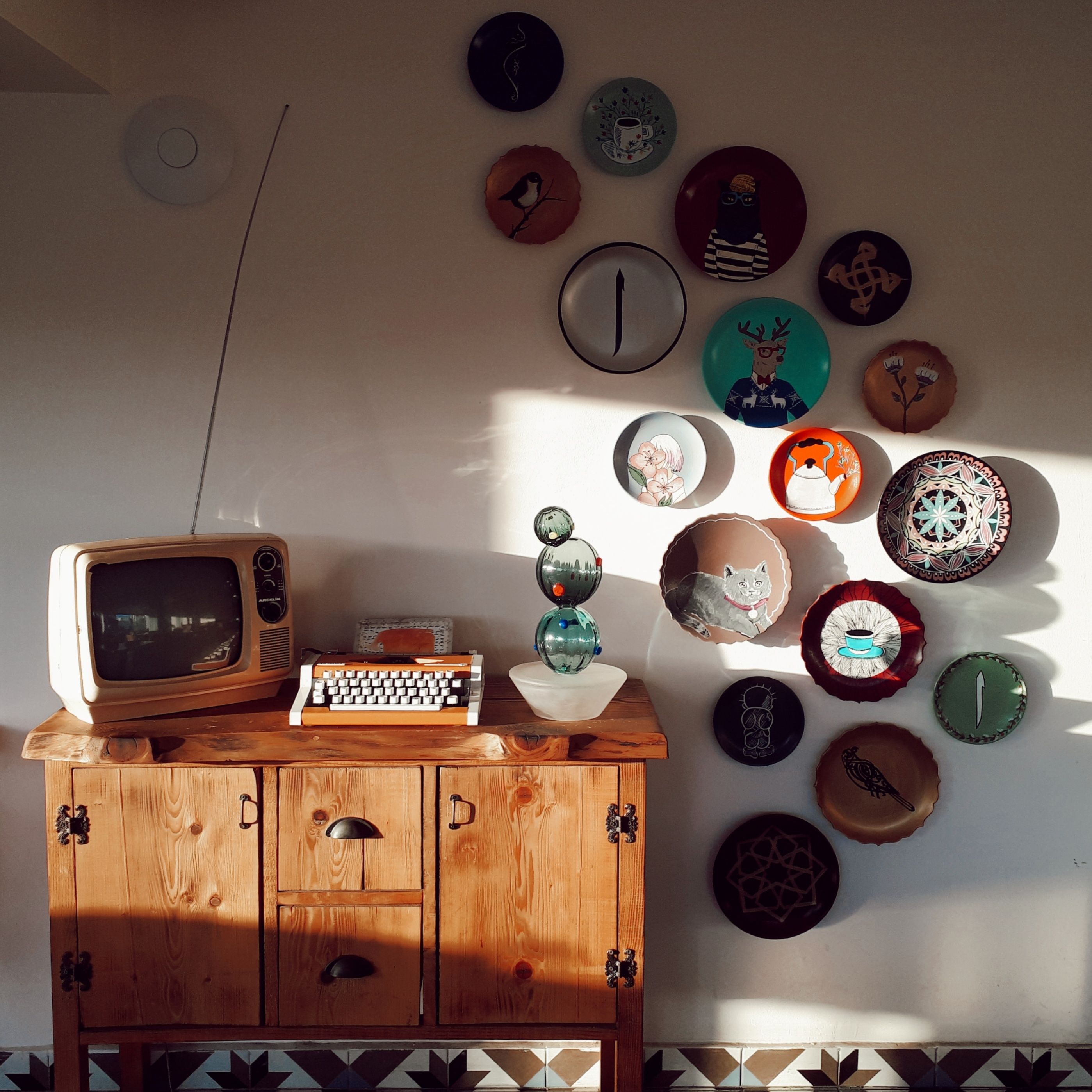 Retro living room setup featuring a vintage TV, typewriter, and decorative wall plates, bathed in warm daylight.
