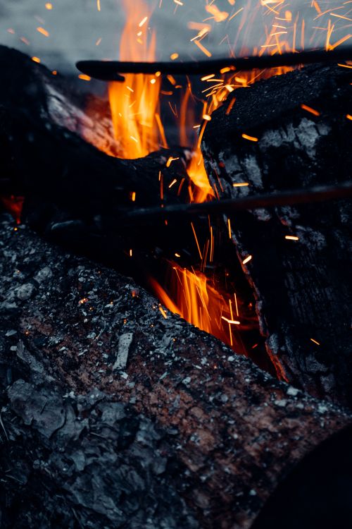 Free Fiery close-up shot of a burning log with vibrant flames and glowing embers, ideal for nature and camping themes. Stock Photo