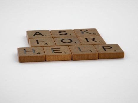Scrabble tiles arranged on a white background forming the phrase 'Ask for Help', conveying a message of communication.