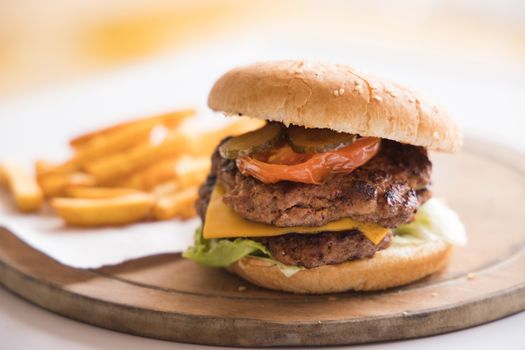 Close-up of a mouthwatering cheeseburger with juicy beef patty and crispy french fries on a wooden plate.