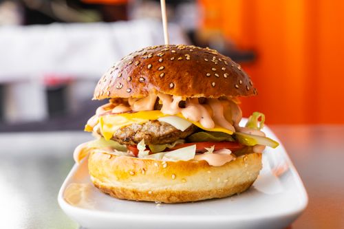 Free Close-up of a mouthwatering cheeseburger with toppings on a white plate. Stock Photo