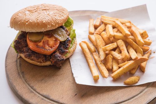 Free Mouthwatering beef burger with fresh toppings and crispy fries served on a wooden tray. Stock Photo