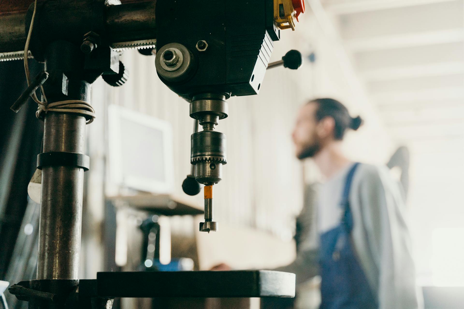 A factory worker stands near machinery in an industrial workshop setting.