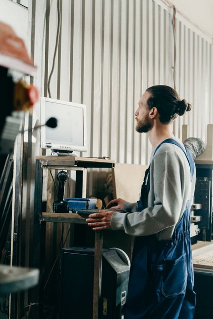 Industrial worker in denim overalls with man bun operates machinery indoors. Industrial worker in denim overalls with man bun operates machinery indoors.