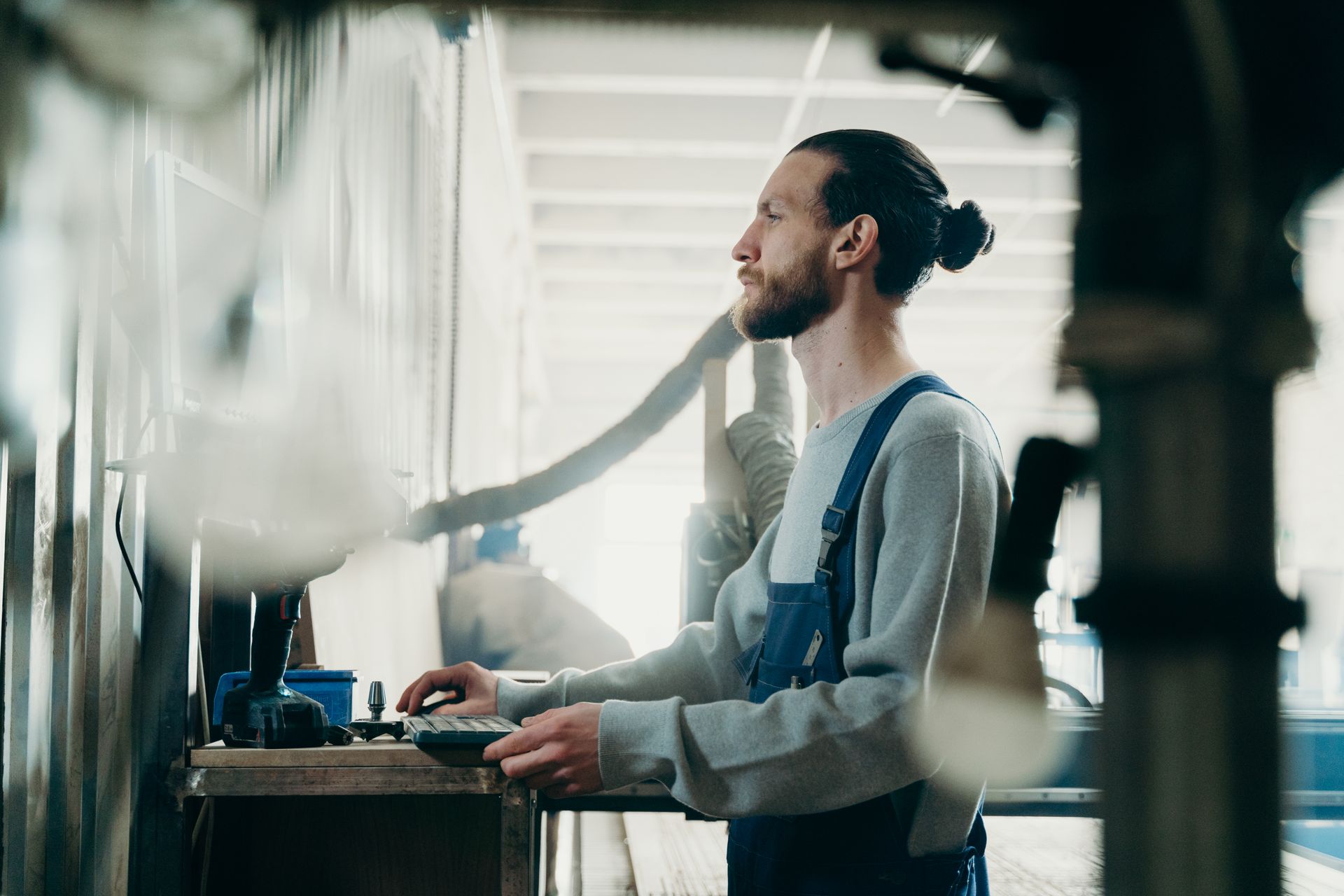 Bearded man with bun focused on his work at a modern industrial workspace.