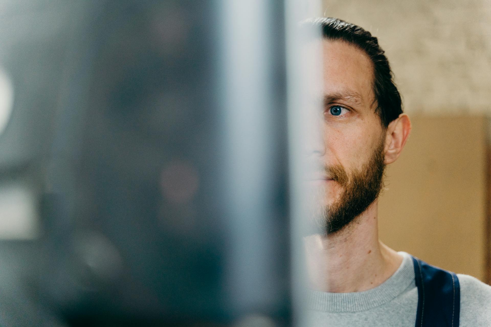 Focused young bearded male employee in casual clothes using computer while working at office