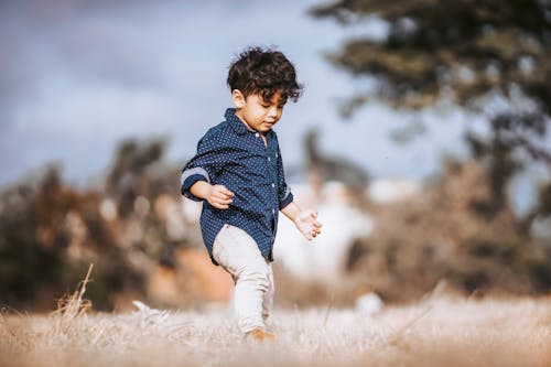 A Boy in Polka Dots Long Sleeves Walking on a Grass Field
