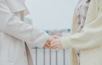 People Wearing Coat and Cardigan Holding Each Others Hand