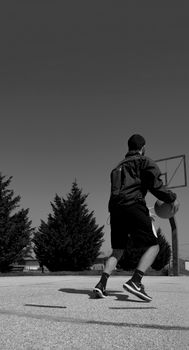 Black and white image of a basketball player practicing on an outdoor court.