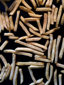 A high-angle shot of golden French fries scattered on a black surface, showcasing their crunchy texture.