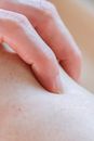 Closeup of crop anonymous person touching delicate skin of leg with hand while standing in light room on blurred background