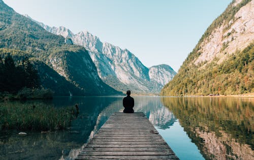 Free A Person Sitting on Wooden Planks Across the Lake Scenery Stock Photo