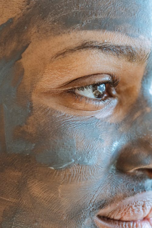 Crop African American female with brown eyes cleansing pores with mud mask and looking away