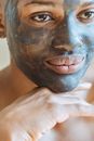 Crop young black female with clay mask applied on face touching chin and looking away