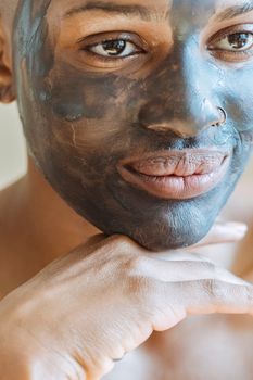 Crop young black female with clay mask applied on face touching chin and looking away