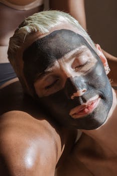 Serene woman with charcoal face mask enjoying a tranquil spa moment.
