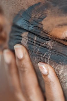 Closeup of crop anonymous African American female touching face with applied mud mask and demonstrating wrinkles on skin