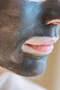 Closeup of crop anonymous female with mud mask on face on blurred background