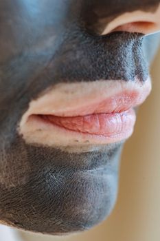 Closeup of crop anonymous female with clay mask on face on beige background