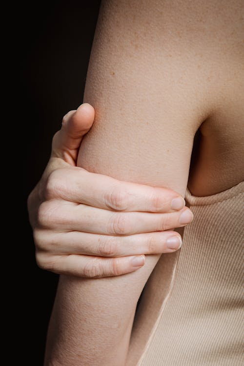 Free Crop anonymous person with bare shoulder and hand holding arm against black background Stock Photo