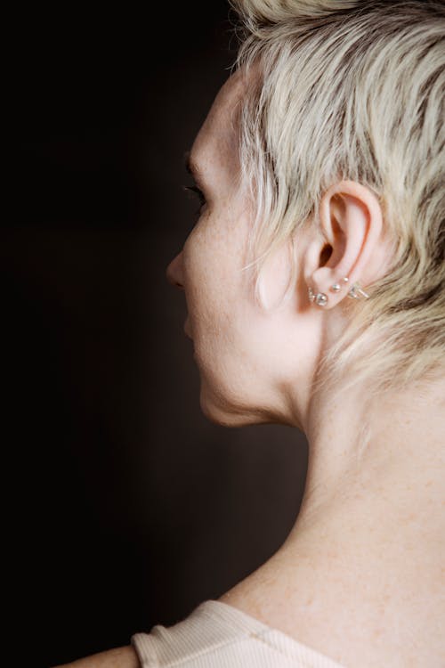 Profile of crop female with short blond hair looking away on dark background