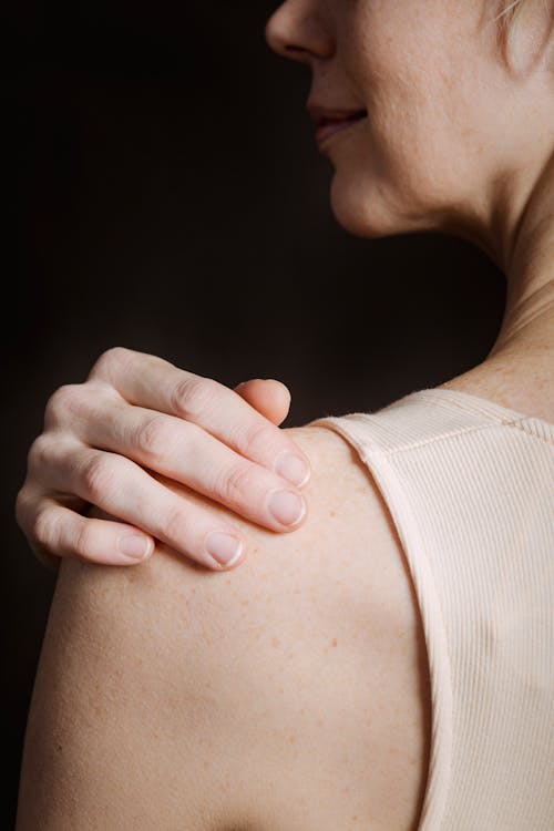 Free Back view of crop unrecognizable woman touching bare shoulder against black background and looking away Stock Photo