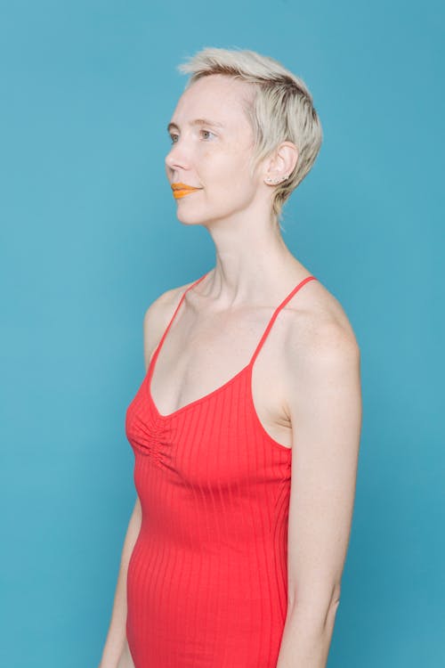 Fair haired woman in red bodysuit standing against blue background and looking away