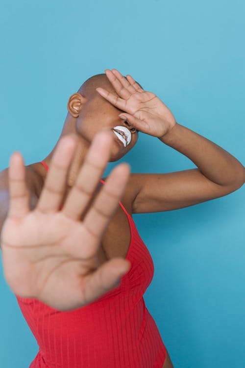Black woman with white lipstick covering eyes with hand and holding out palm to camera in stopping gesture