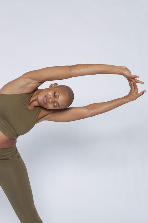 African American female in sportswear with closed eyes bending aside and straightening arms on white background