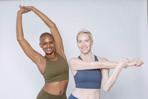 Free Cheerful multiracial fit females in sportswear smiling and looking at camera while standing against white background and stretching arms Stock Photo